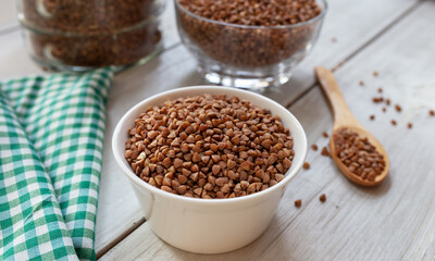 Bowl of raw buckwheat with spoon on wooden background