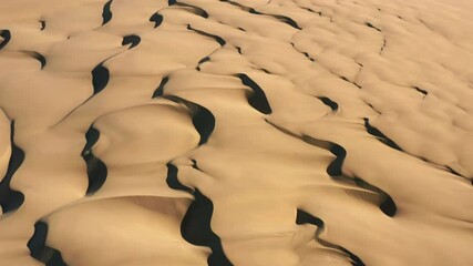 Inspiring aerial shot of an endless beige-golden texture of sand dunes at sunset. 4K vertical drone shot of desert nature, perfect for background and commercial use. Deep shadows create waving texture - Powered by Adobe