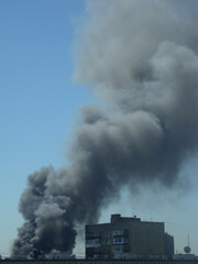 Black smoke from the fire over the city. A pillar of smoke above the house in the blue sky.