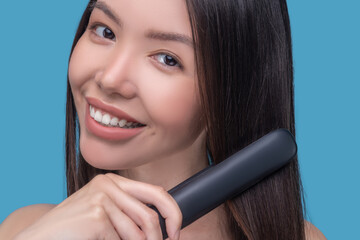 Smiling young dark-haired woman straightening her hair