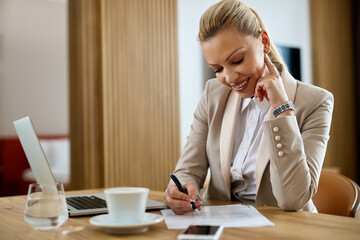 Smiling businesswoman writing reports while working in a hotel room.