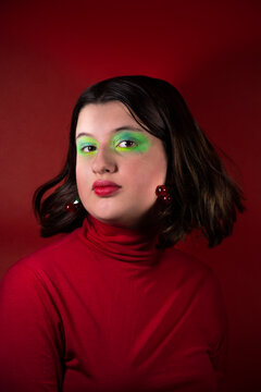 Modelo con maquillaje verde y pelo casta&ntilde;o mirando a c&aacute;mara con fondo y remera roja  