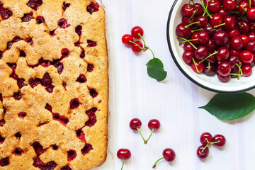 Homemade biscuit cherry pie and cherry berries in a bowl on a white tablecloth. Freshly baked cherry cake on the table. Flat lay, top view.