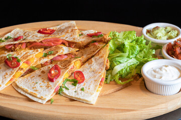 Pita stuffed with vegetable and meat mixture. Garnished with peppers. The dish includes vegetable, avocado and garlic dip in white bowls. The food is isolated on a black background