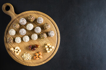 Raw vegetarian energy balls with cashews, hazelnuts, peanut butter and almond in the wooden board on the dark background. Vegetarian, organic food. Flat lay, close up, copy space.