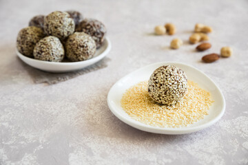 Energy ball close up. The candy is sprinkled with sesame. Homemade raw sweet with almond, cashews, peanut butter and hazelnuts on the plate on the light background. Vegetarian snack.