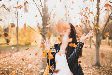 Cheerful happy girl waving her hands from falling autumn leaves - a gust of wind raised the foliage - joy and good mood
