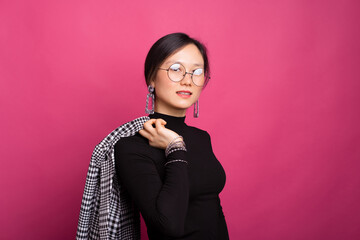 Portrait of a young woman wearing glasses holding her jacket over pink background
