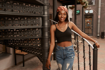 Young beautiful stylish african woman standing and posing. Girl in jeans and black shirt. Outdoor summer fashion lifestyle portrait.