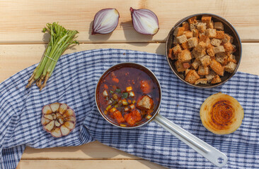 Homemade thick soup in a ladle and a bowl of rye bread crackers on a blue napkin. top view, horizontal orientation