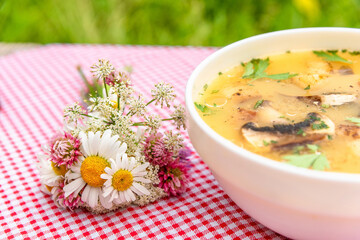 Soup with mushrooms in the open air and a small bouquet of wild flowers. Vegetarian lunch.