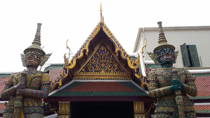 Naklejka premium Demonios protectores budistas junto a una entrada decorada artísticamente en un templo en Bangkok, Tailandia.