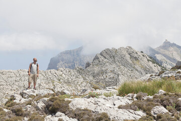 A photographer on the top of the mountains of Mallorca during the summer holidays. Spectacular panoramic views. The man is using a professional camera and carries a backpack