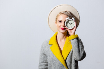 Blonde girl in grey coat and vintage hairdress with alarm clock