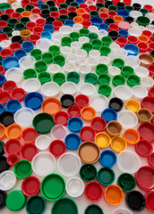 Close up of collage with colorful plastic bottle caps and recycling sign on white background. Reuse of waste concept.