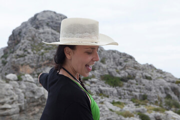 A young woman walking down a mountain road on the island of Majorca. The woman is wearing a cowboy hat and a black and green jacket. The woman is enjoying the summer holidays. Panoramic views Majorca