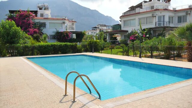 Beautiful rectangular outdoor pool with blue turquoise water and a villa with green trees and flowers, on a background of mountains. Concept of summer vacation and solitude in nature without people