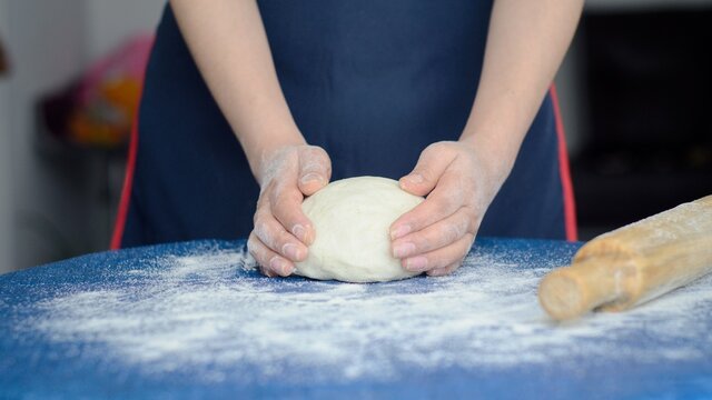 Manos de mujer amasa la masa cruda sobre una mesa azul. Panadero prepara masa para hacer pasteles, pizzas o pastas.