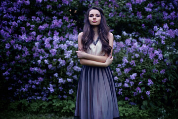 Obraz na płótnie Canvas Fashion portrait of young beautiful pretty girl posing against lilac bushes in blossom