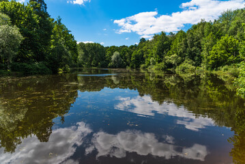 Summer forest landscape - sky with clouds reflected in the water of a forest lake in a national park