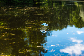 Soap bubble flying over the forest lake and the sky is reflected in it, the water and trees