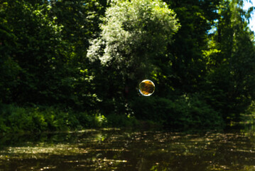Soap bubble flying over the forest lake and the sky is reflected in it, the water and trees