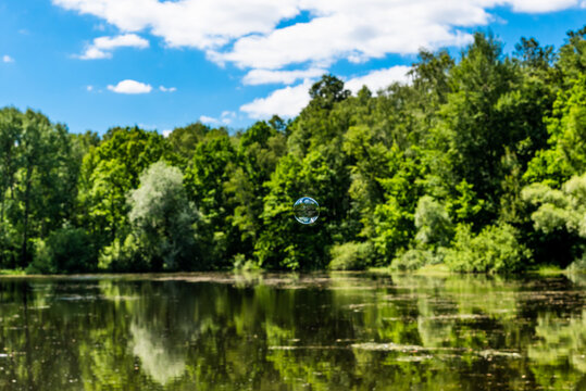 Soap bubble flying over the forest lake and the sky is reflected in it, the water and trees