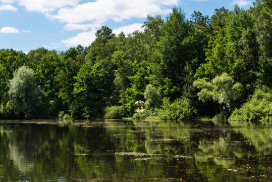 Soap bubble flying over the forest lake and the sky is reflected in it, the water and trees