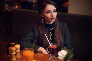 Young beautiful pretty stylish dressed formal woman looking away and drinking mulled wine