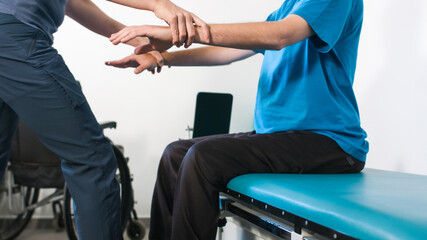 Physiotherapist exercising with disabled person using wheelchair on a therapy table.