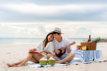 Asian couple happy and enjoy the trip honeymoon of couple lover on the sea beach by playing Ukulele...
