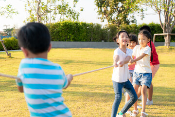 Fototapeta premium Group of happy young Asian children playing tug of war or pull rope togerther outside in city park playground in summer day. Children and recreation concept..
