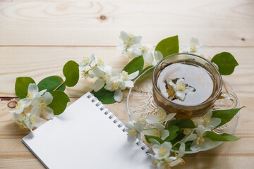 a cup of green tea and Jasmine flowers on a white background top view. morning tea and an empty notebook with on the table. copy space. the cup and flowers lay flat.
