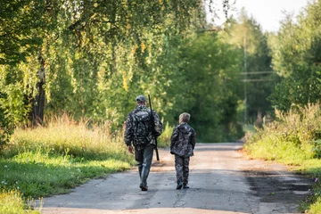 Poster Father and son hunting together. Walking the road after the bird hunt. © romankosolapov
