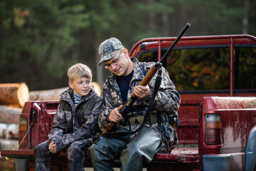 The smiling hunter or military person with gun or rifle and his apprentice in summer forest during...