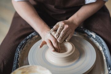 Close-up view of woman hands working on pottery wheel and making clay pot. Hands sculpts a cup from clay pot. Workshop on modeling on the potter's wheel