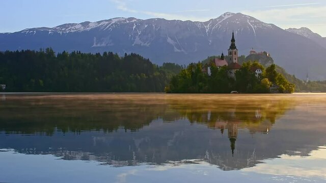 Beautiful morning at Lake Bled and Julian Alps in the background. The lake island and charming little church dedicated to the Assumption of Mary are famous tourist attraction in Slovenia.
