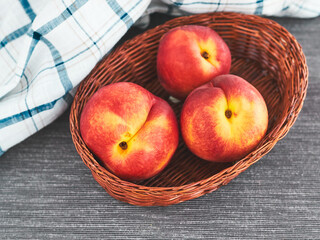 Ripe juicy organic nectarines (peaches) in a wicker basket on the grey table with white napkin. Top view