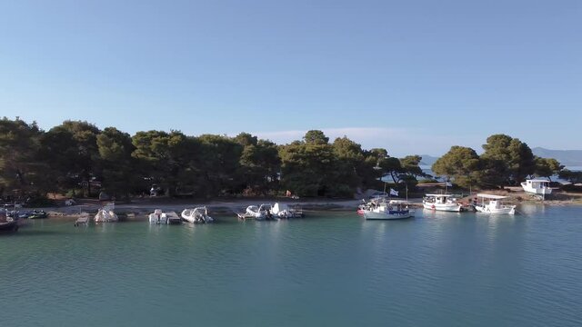 Drone flying above caique fishing boats, leading to calm sea. Aerial top view of Glarokavos lagoon at Kassandra Chalkidiki peninsula shoreline with green plantation.