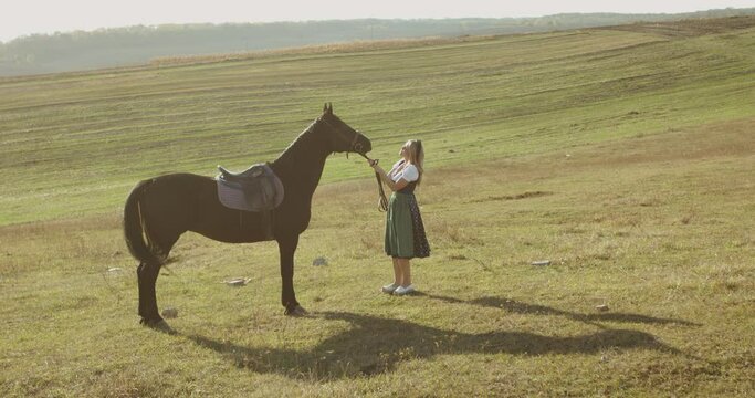 Woman in a dress has a fun and caresses a brown horse among the wide steppes