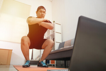 Fototapeta na wymiar Asian male doing exercise at home while watching online video instruction on laptop, indoor home workout, keep healthy on new normal lifestyle
