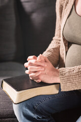Pregnant Woman Praying at Home with Hands over a Bible