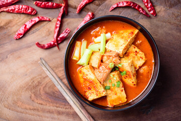 Kimchi soup with tofu and pork in a bowl on wooden background, Korean food (Kimchi Jjigae)	