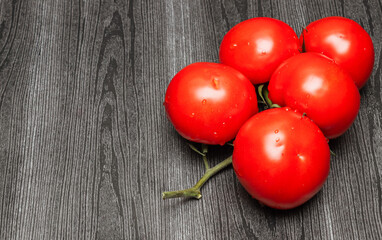 ripe tomatoes on a branch on the left on a black wooden table and with place for text on the right, closeup side view.