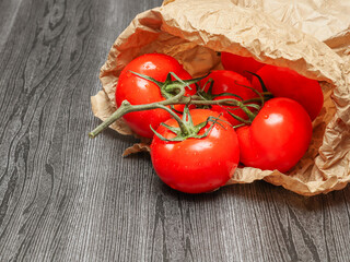 ripe tomatoes on a twig in a paper bag on the left on a black wooden table, closeup side view.