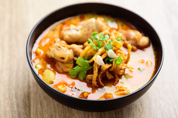 Northern Thai food (Khao Soi), Spicy curry noodles soup with coconut milk and chicken in a bowl on wooden table
