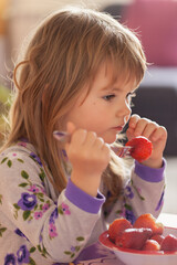 Adorable little girl in pajama eating strawberries at home