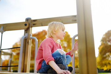 Cute preschooler boy having fun on outdoor playground. Spring/summer/autumn active sport leisure for kids.