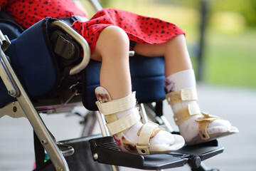 Disabled girl sitting in wheelchair. On her legs orthosis. Child cerebral palsy. Disability....