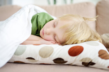 Afternoon sleep of preschooler or elementary school child. Tired boy fell asleep on sofa in the afternoon. Baby having a day nap. Parents overloads children with learning and activities.